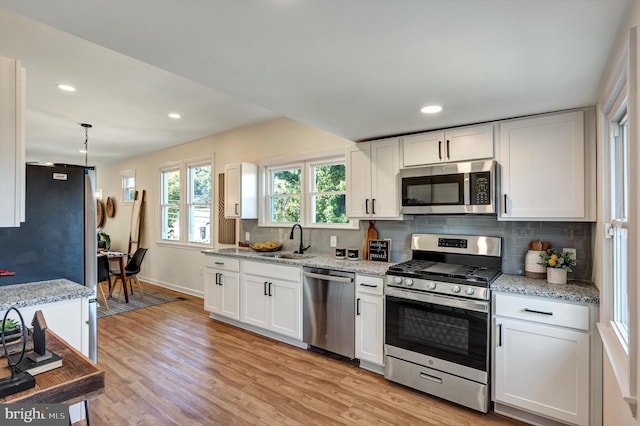 kitchen with light stone counters, stainless steel appliances, light wood-type flooring, and white cabinetry