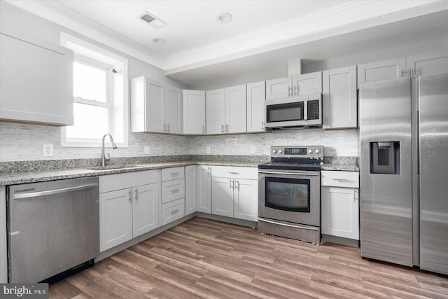 kitchen with appliances with stainless steel finishes, white cabinetry, light hardwood / wood-style floors, sink, and ornamental molding