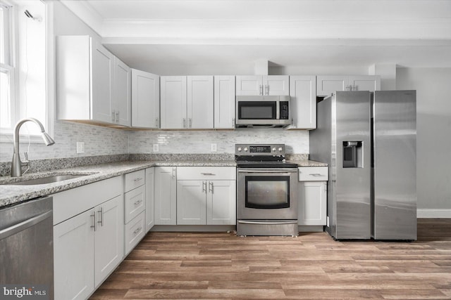 kitchen with sink, white cabinetry, light wood-type flooring, light stone countertops, and appliances with stainless steel finishes