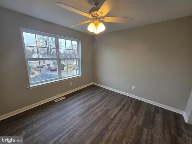 spare room featuring dark wood-style floors, baseboards, visible vents, and a ceiling fan