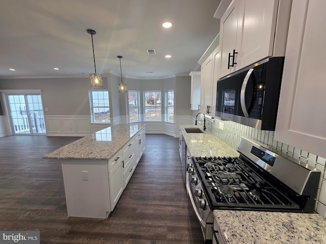 kitchen with gas stove, a sink, white cabinets, crown molding, and a center island