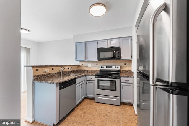 kitchen with appliances with stainless steel finishes, dark stone countertops, a peninsula, gray cabinetry, and a sink