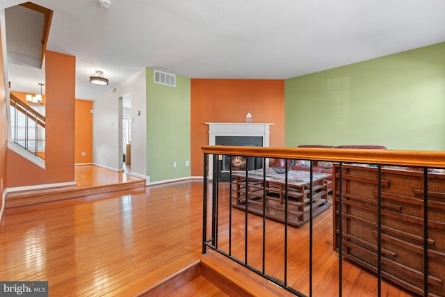 stairway featuring a warm lit fireplace, baseboards, visible vents, and hardwood / wood-style floors