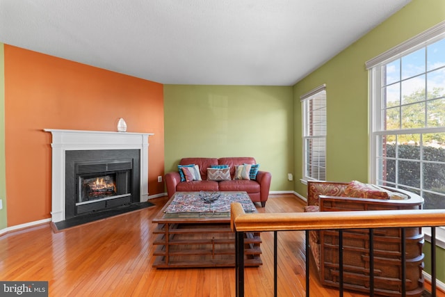 living area with a fireplace with flush hearth, wood-type flooring, and baseboards