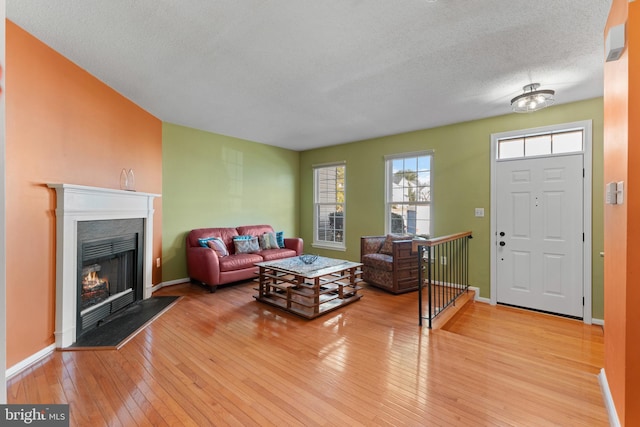 living room featuring a textured ceiling, a lit fireplace, light wood-type flooring, and baseboards