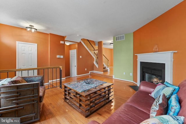 living area with wood-type flooring, visible vents, a fireplace with flush hearth, baseboards, and stairs