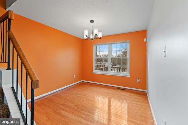 unfurnished dining area featuring visible vents, baseboards, stairs, hardwood / wood-style floors, and an inviting chandelier