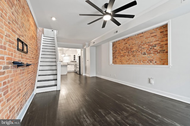 unfurnished living room with ceiling fan, dark hardwood / wood-style flooring, and brick wall