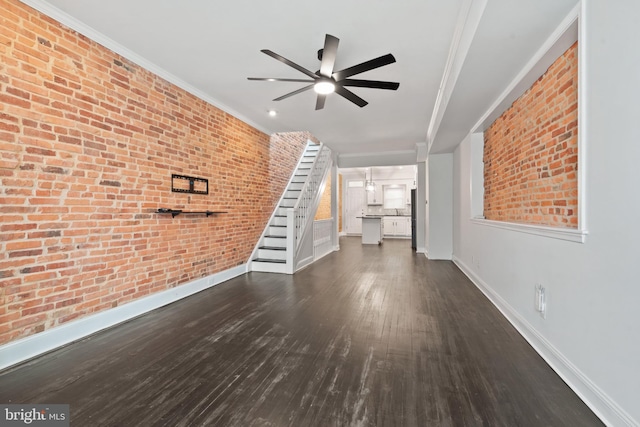 unfurnished living room with crown molding, ceiling fan, dark wood-type flooring, and brick wall