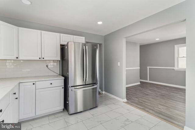 kitchen with tasteful backsplash, light stone counters, stainless steel refrigerator, and white cabinets