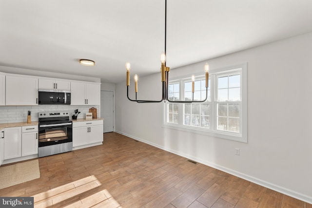 kitchen with appliances with stainless steel finishes, light hardwood / wood-style floors, pendant lighting, white cabinetry, and tasteful backsplash