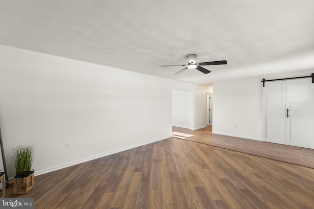 unfurnished bedroom with ceiling fan, a barn door, and dark hardwood / wood-style floors