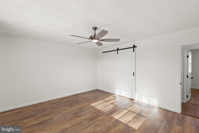 empty room featuring ceiling fan, dark wood-type flooring, and a barn door