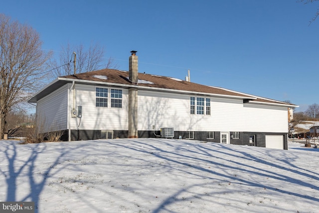 snow covered back of property featuring central air condition unit and a garage