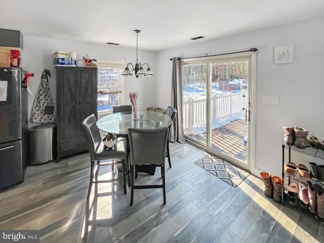 dining space featuring a healthy amount of sunlight, wood-type flooring, and an inviting chandelier