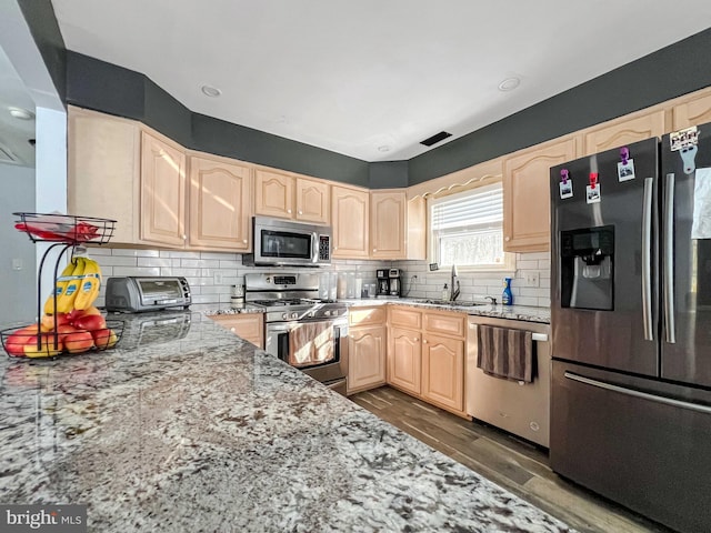 kitchen with light stone countertops, sink, stainless steel appliances, dark wood-type flooring, and light brown cabinetry