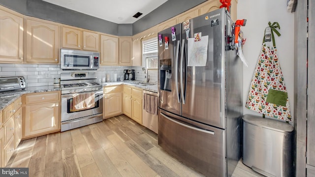 kitchen with sink, light wood-type flooring, light brown cabinetry, appliances with stainless steel finishes, and light stone counters