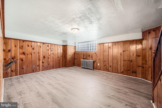 additional living space featuring wooden walls, hardwood / wood-style floors, radiator, and a textured ceiling