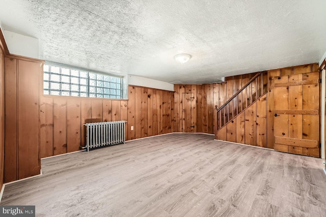 unfurnished room with radiator heating unit, light wood-type flooring, a textured ceiling, and wooden walls