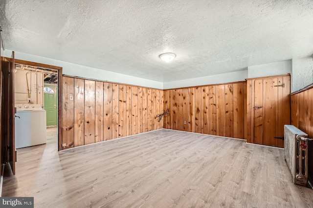 interior space featuring washer / clothes dryer, wooden walls, a textured ceiling, and light wood-type flooring