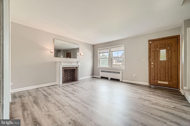 unfurnished living room featuring radiator, a fireplace, and light wood-type flooring