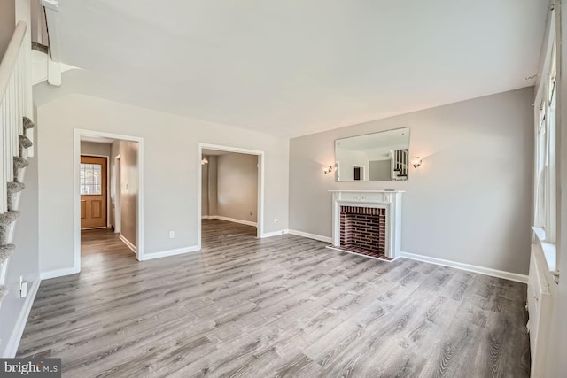 unfurnished living room featuring light hardwood / wood-style flooring and a brick fireplace