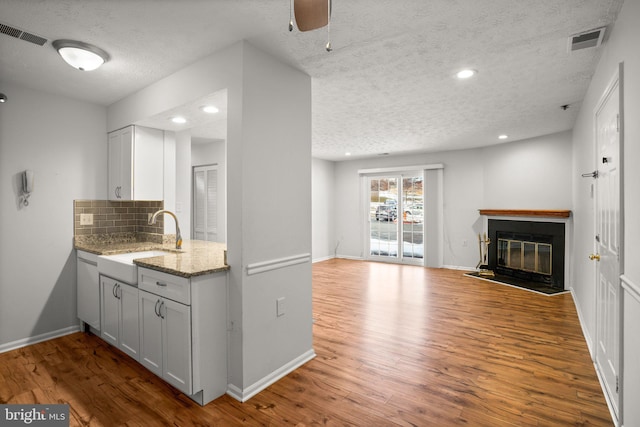 kitchen featuring light stone counters, a textured ceiling, tasteful backsplash, white cabinetry, and sink