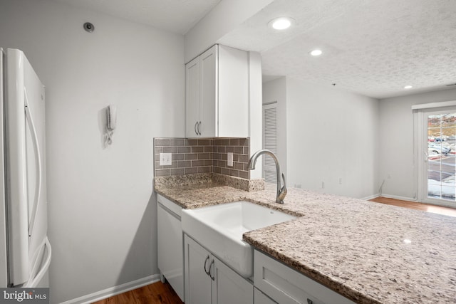 kitchen featuring light stone countertops, white fridge, decorative backsplash, white cabinetry, and sink