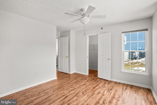 unfurnished bedroom with a textured ceiling, a closet, light hardwood / wood-style floors, a walk in closet, and ceiling fan