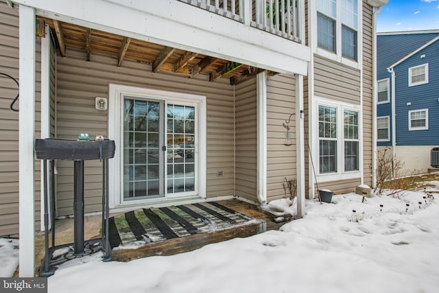 snow covered property entrance with central AC and a balcony