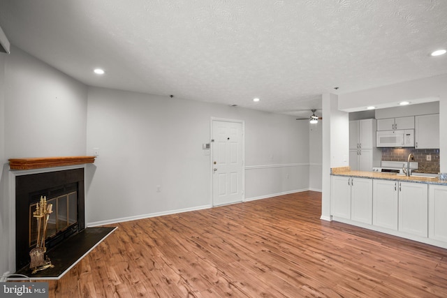 unfurnished living room featuring sink, a textured ceiling, light wood-type flooring, and ceiling fan