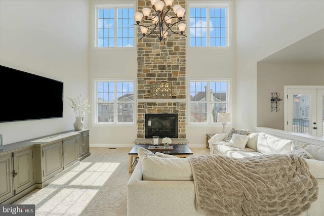 carpeted living room with an inviting chandelier, a wealth of natural light, a towering ceiling, and a stone fireplace