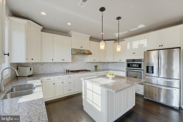 kitchen with appliances with stainless steel finishes, white cabinets, hanging light fixtures, a kitchen island, and light stone counters