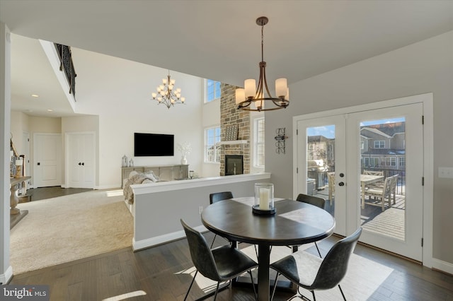 dining area featuring dark hardwood / wood-style floors, a healthy amount of sunlight, a stone fireplace, and an inviting chandelier