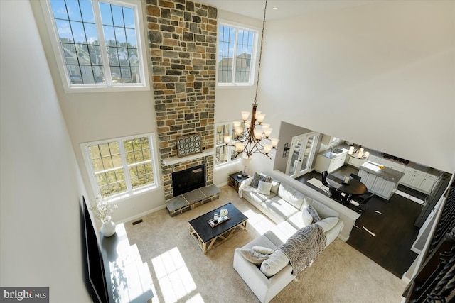 living room featuring a wealth of natural light, a notable chandelier, a towering ceiling, and a fireplace