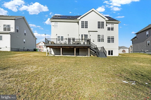 rear view of property featuring a deck, a lawn, and solar panels