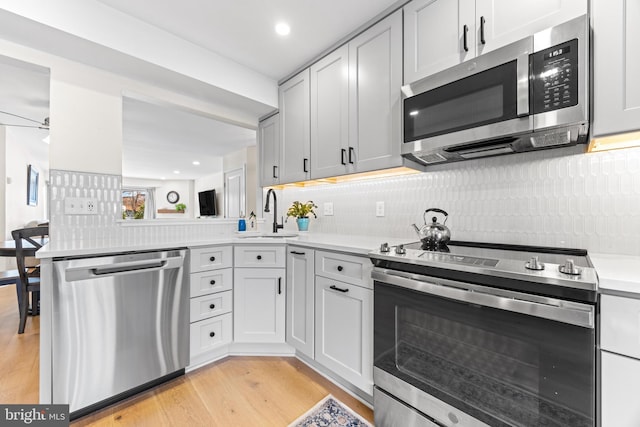 kitchen featuring kitchen peninsula, light hardwood / wood-style flooring, stainless steel appliances, tasteful backsplash, and sink