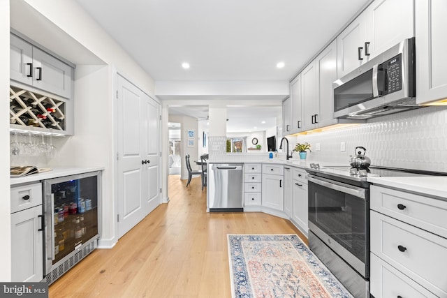 kitchen featuring stainless steel appliances, wine cooler, light hardwood / wood-style floors, and white cabinetry