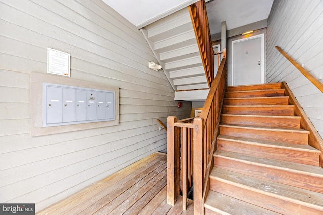 stairway with a mail area, wooden walls, and vaulted ceiling