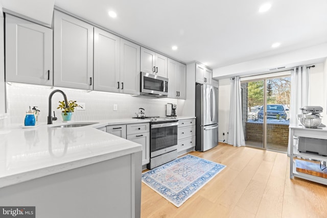 kitchen featuring light hardwood / wood-style floors, stainless steel appliances, light stone counters, sink, and tasteful backsplash