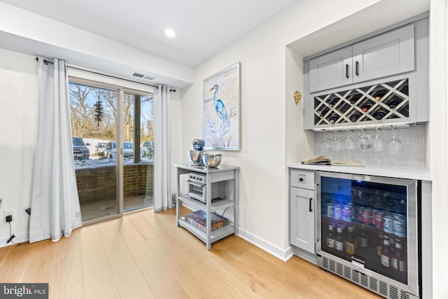 bar featuring light hardwood / wood-style flooring, decorative backsplash, and wine cooler