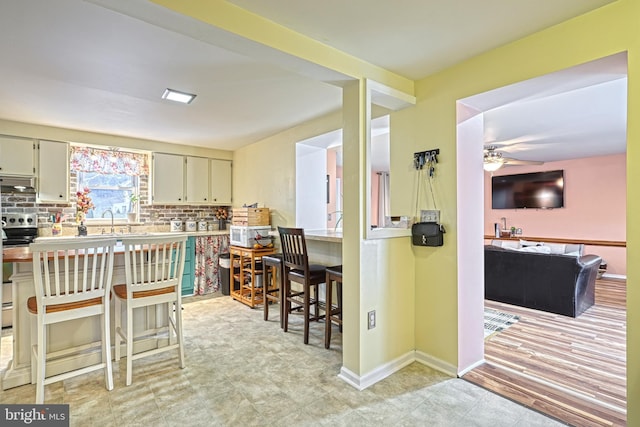 kitchen with stainless steel electric stove, backsplash, ceiling fan, and a breakfast bar