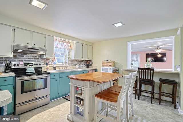 kitchen with electric range, ceiling fan, sink, backsplash, and a breakfast bar