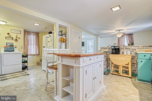 kitchen with ceiling fan, white fridge, washer / dryer, a breakfast bar area, and white cabinets