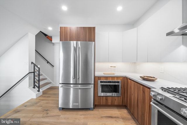 kitchen featuring white cabinets, light hardwood / wood-style flooring, wall chimney exhaust hood, and stainless steel appliances