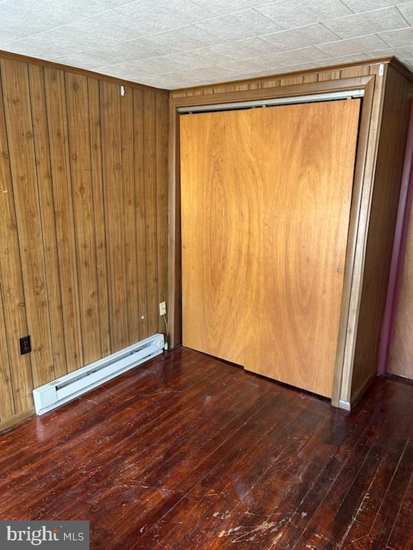 spare room with wood walls, dark hardwood / wood-style flooring, and a baseboard radiator