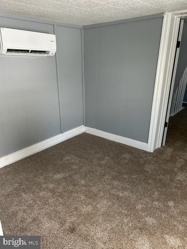 spare room featuring a wall mounted air conditioner and dark colored carpet