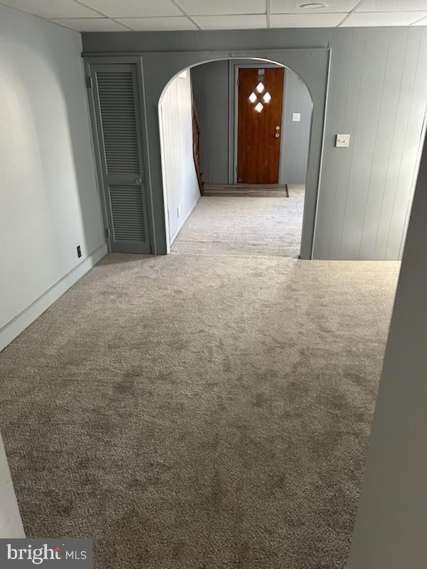 spare room with a paneled ceiling, light colored carpet, and wooden walls