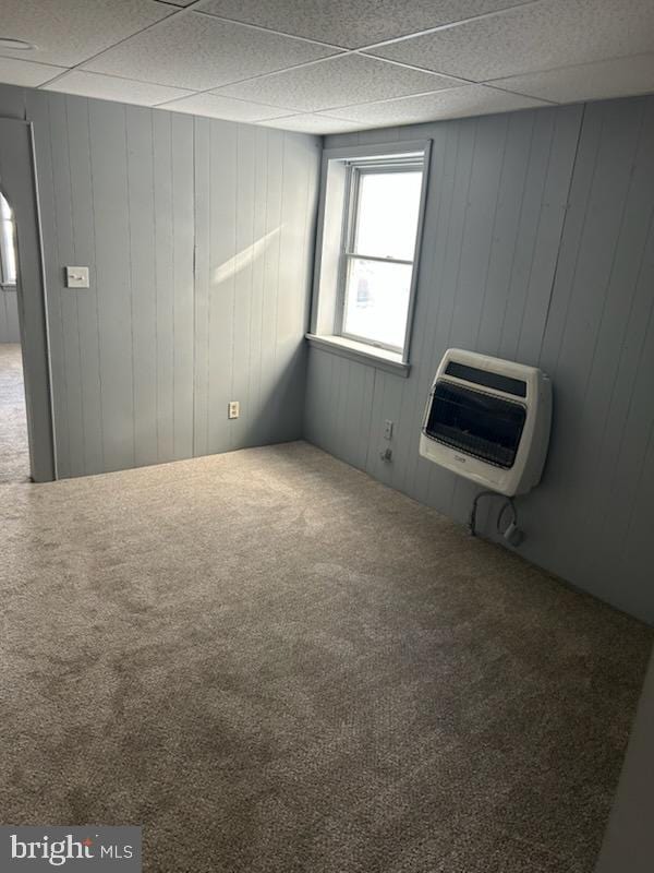 carpeted empty room featuring wooden walls and heating unit