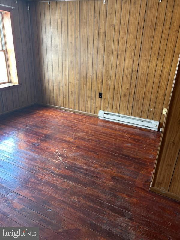 empty room with dark hardwood / wood-style floors, wooden walls, and a baseboard radiator